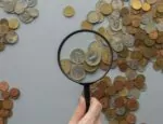 hand holding magnifying glass over coins