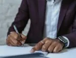 man in purple suit writing on white paper with black pen