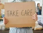 person holding brown cardboard sign with words "take care"
