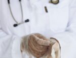 clinician in white coat with stethoscope and gloves