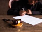 judge signing a law next to a wooden gavel mallet